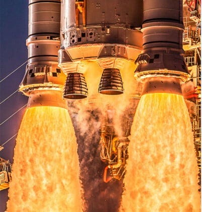 Close-up of rocket engines firing with bright flames and smoke on the left; wide view of a rocket launching, rising above a launch pad with clouds of smoke and blue sky on the right.