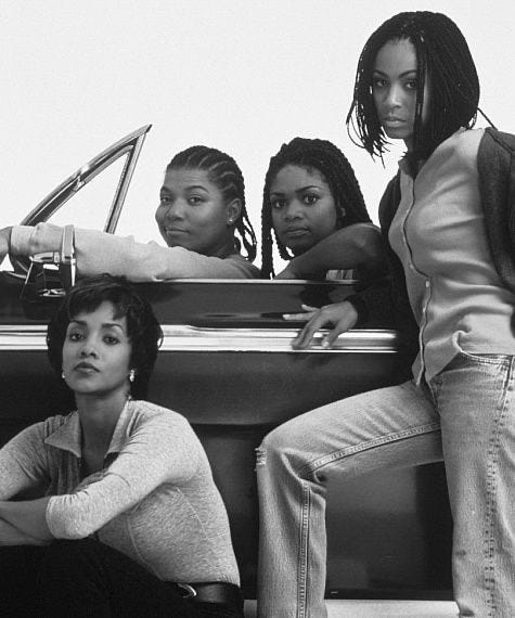 This may contain: four young women sitting on the back of a car in front of a man standing next to them