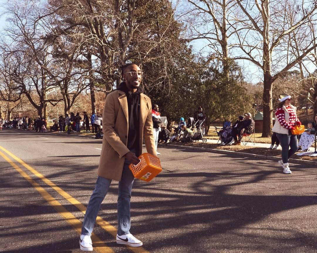 Doughty  in a coat and hat stands on the street during a city event
