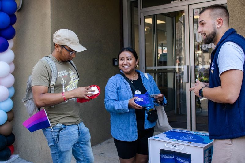 From left to right, a man in a beige hat with a pride flag in his pocket looks at one of the kits available in the harm reduction kiosk in front of Hudson Pride Center in Union City, a woman in a denim shirt also looks at another kind of kit available in the kiosk, and a man in a blue vest looks on. From left to right, a man in a beige hat with a pride flag in his pocket looks at one of the kits available in the harm reduction kiosk in front of Hudson Pride Center in Union City, a woman in a denim shirt also looks at another kind of kit available in the kiosk, and a man in a blue vest looks on.