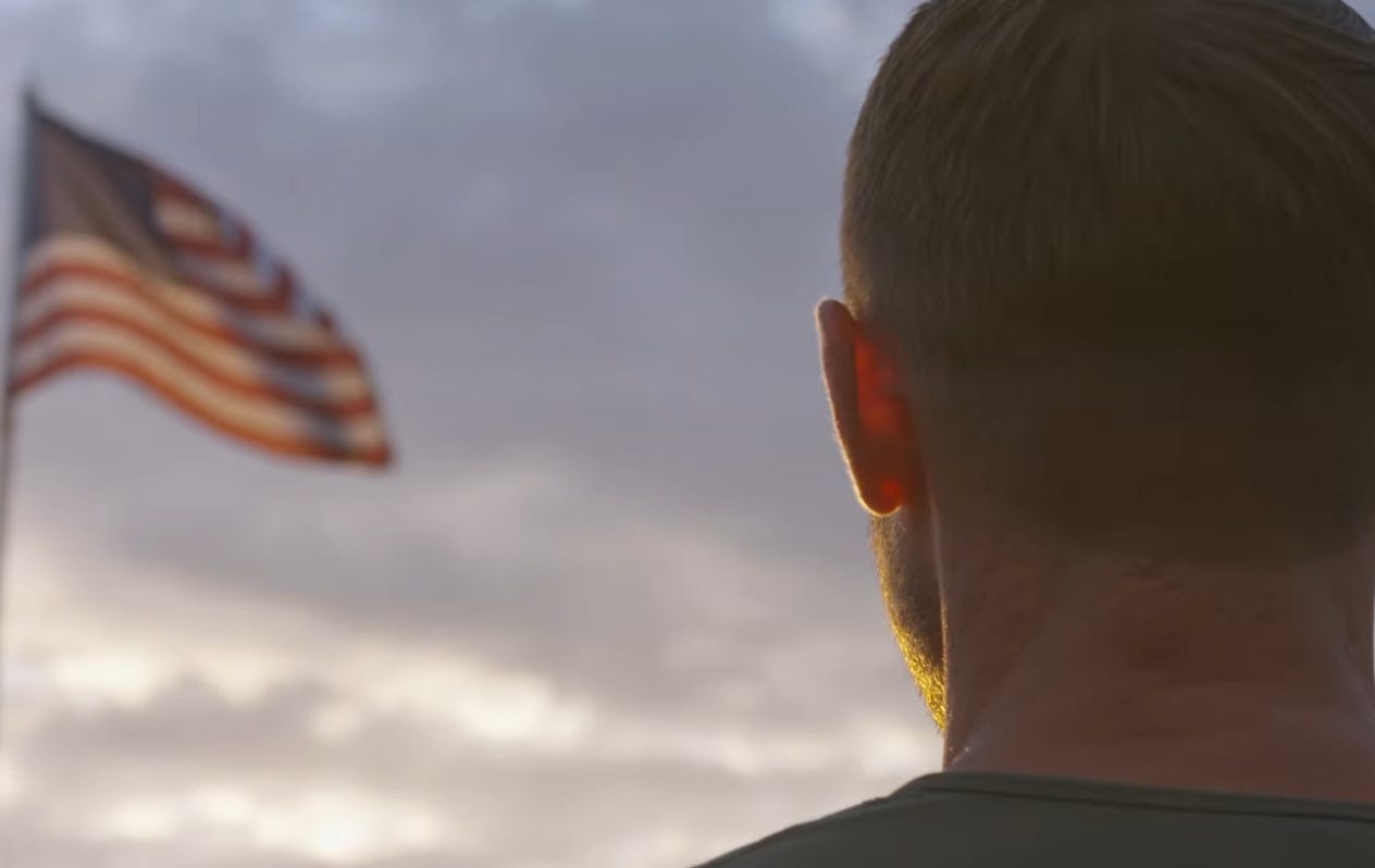 A man with the back of his head to the camera looks at a USA flag