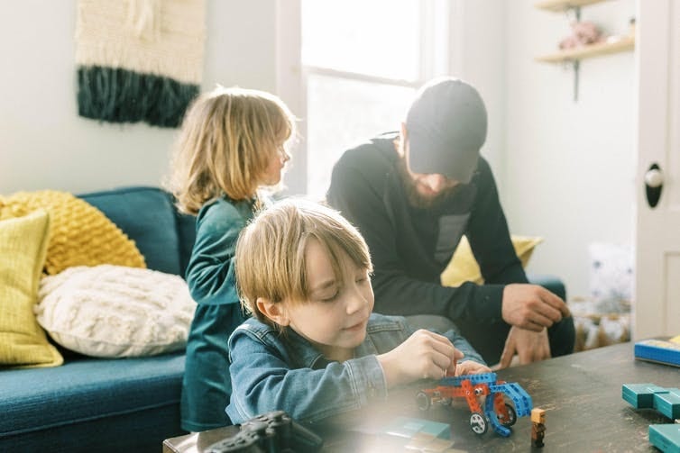 A little boy plays at a table at home with his sister and father nearby A little boy plays at a table at home with his sister and father nearby