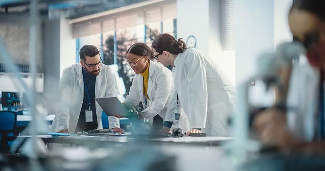 Scientists and engineers collaborating in a lab over a laptop, symbolizing deep-tech startup founders addressing technical feasibility risk.
