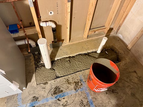 Three photos of a basement renovation in progress. The first shows plumbing pipes set in fresh concrete, the second shows an insulated orange pipe, and the third shows a framed wall with insulation and electrical wiring installed.