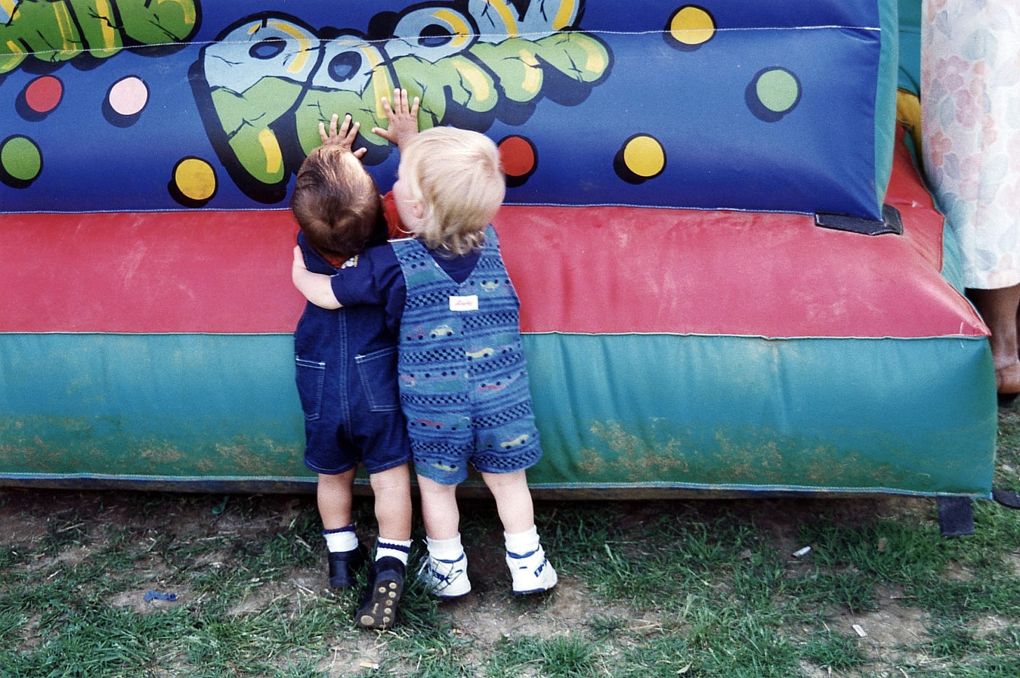 two toddlers hugging and putting their hands on a bouncy house