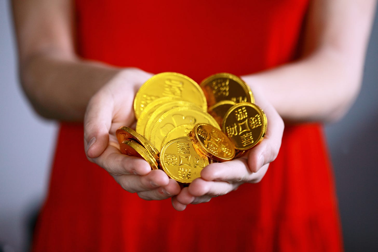 Photo of a woman in a red dress holding gold coins in both her hands