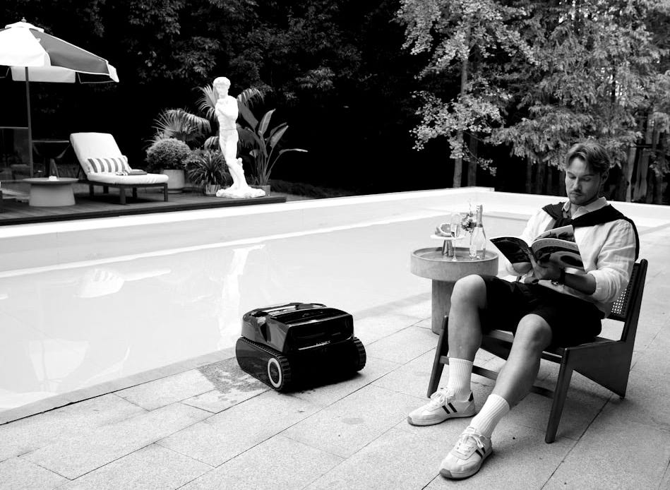 Man reading by pool with robotic lawnmower