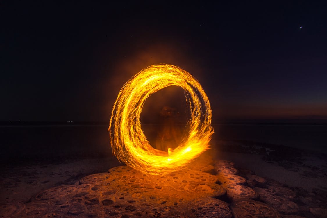 Free Captivating long exposure shot of a fire dancer creating fiery circles on a serene beach at night. Stock Photo