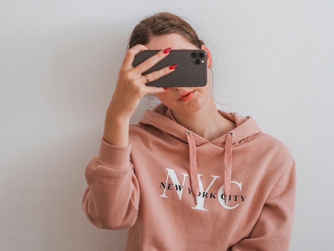 woman in pink hoodie holding an iPhone up to her face