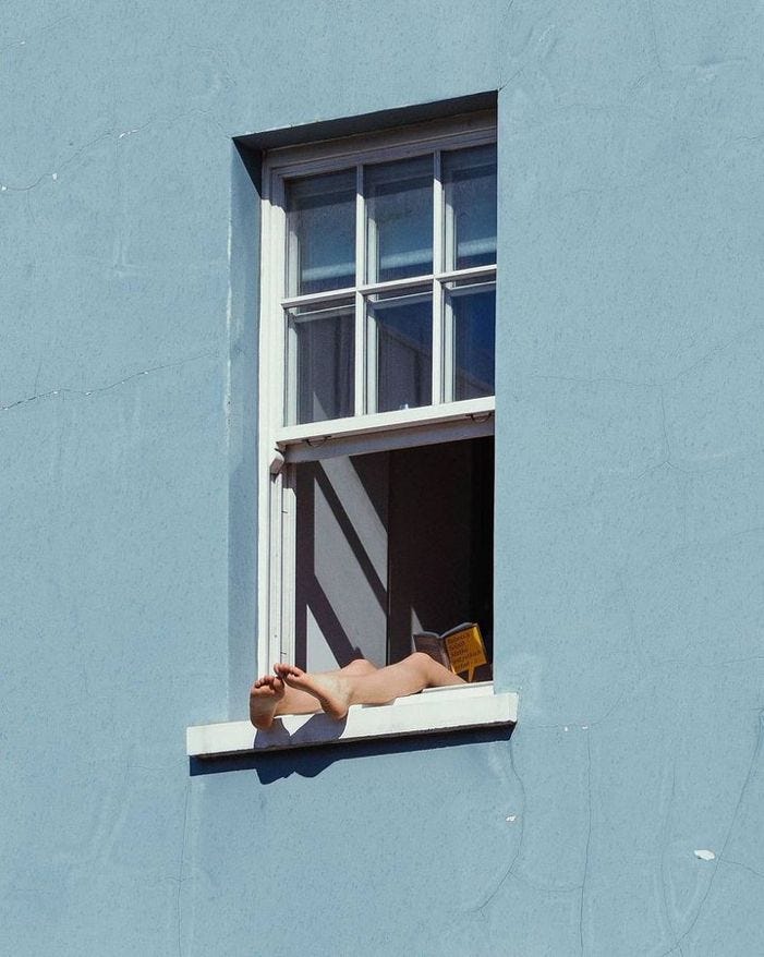 This may contain: a woman laying on the window sill in front of a blue building