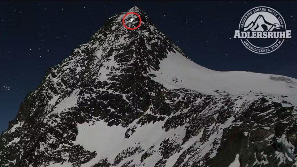 A high angle view of a snow-covered mountain at night, with a red circle around the top where there is a small, illuminated building or tent.