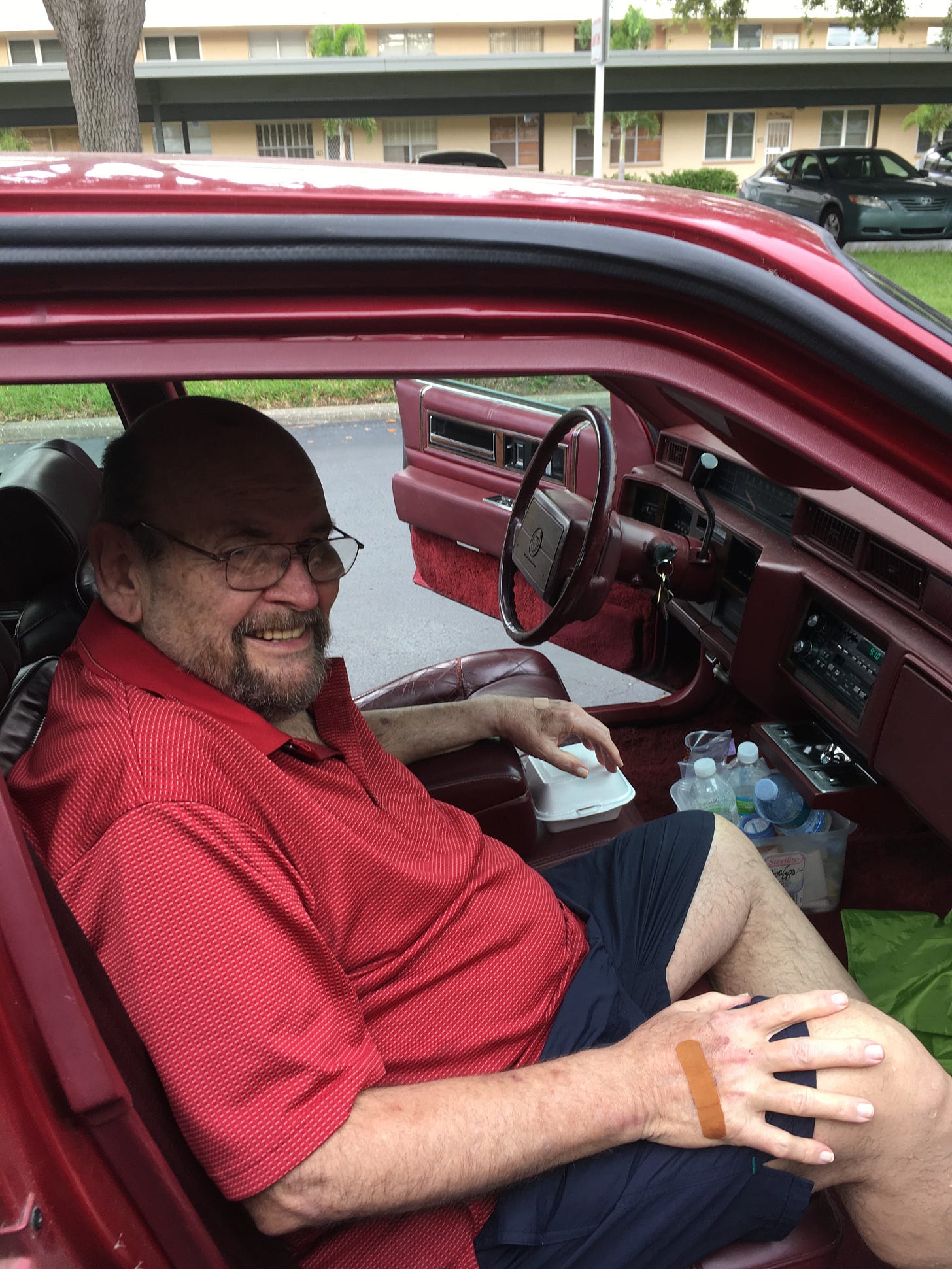 An elderly man sits, smiling, in the passenger seat