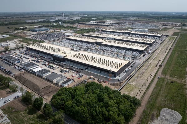 Giant buildings with white roofs are surrounded by farmland.