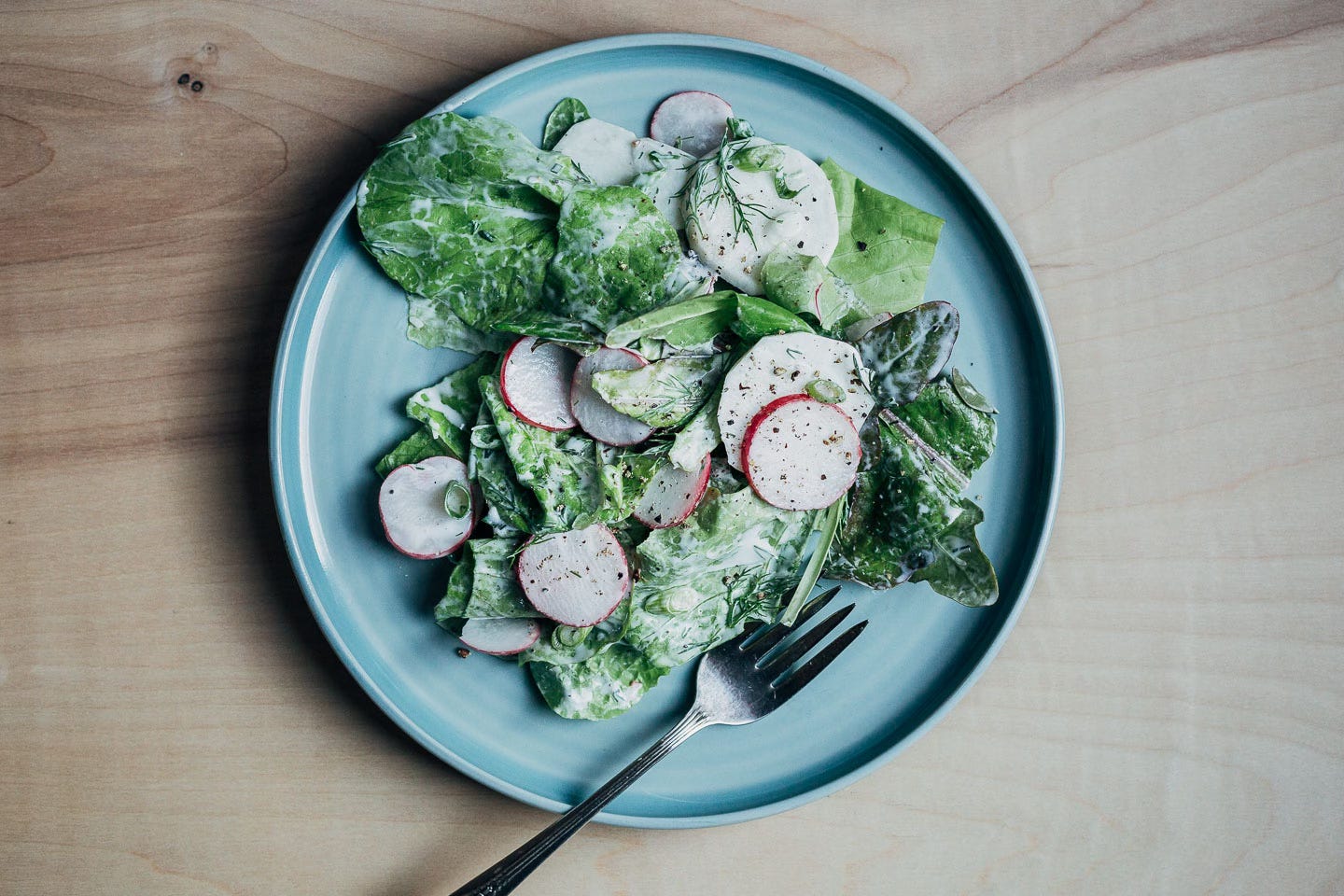 A plate of salad with radishes, turnips, lettuce, and creamy dressing. 