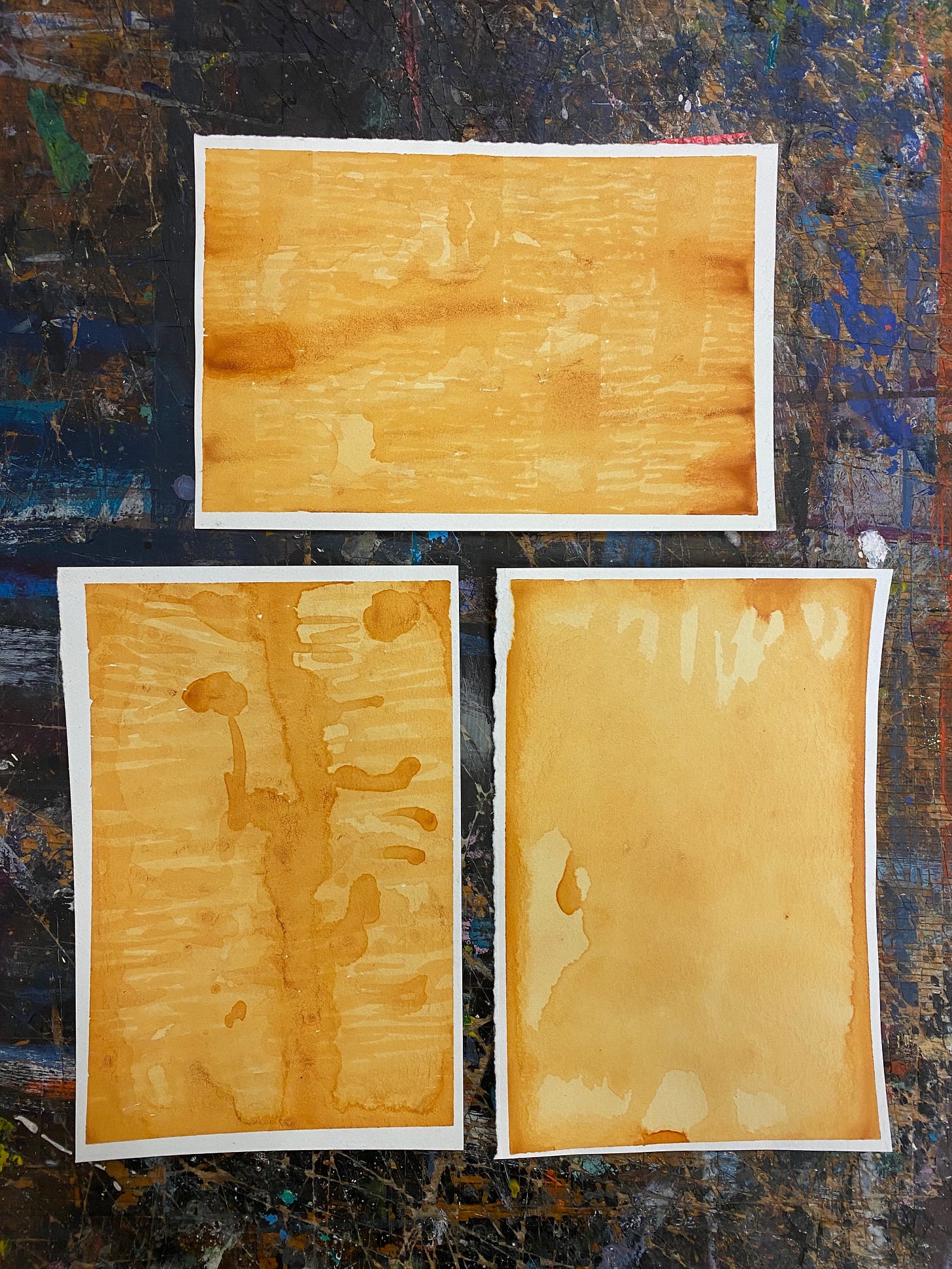 Three rectangular pieces of paper painted with yellow/orange onion skin ink, with lots of abstract swirls, layers, lines, and blobs.