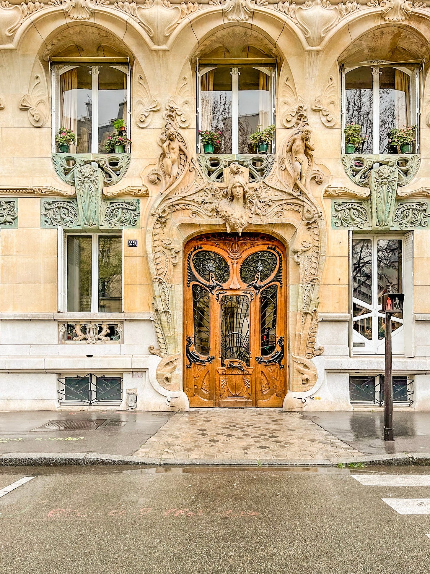 Art Nouveau apartment entrance in Paris with an ornate carved stone façade, sculptural figures, decorative ironwork, and an intricate wooden doorway.
