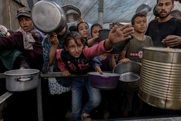 Palestinian children crowding together and reaching out with food containers.