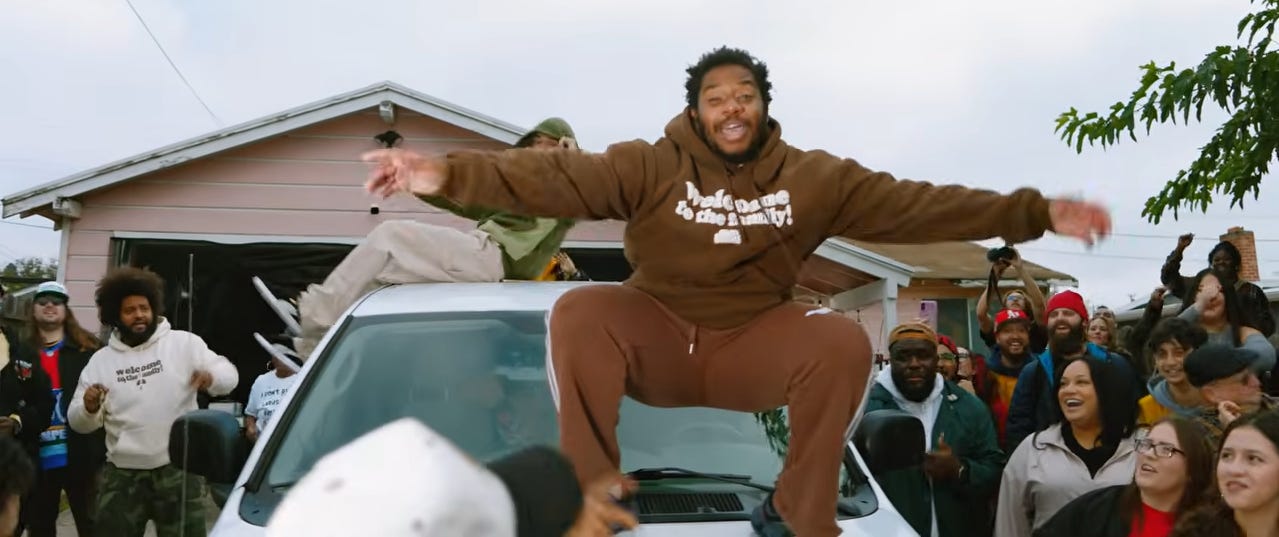 Artist La russell in brown jumpsuit rapping on top of sedan in the bay area