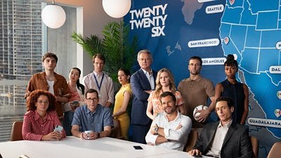 The cast of Twenty Twenty Six stand and sit around a large with a blue map on a wall behind them, featuring cities involved in the football tournament The cast of Twenty Twenty Six stand and sit around a large with a blue map on a wall behind them, featuring cities involved in the football tournament