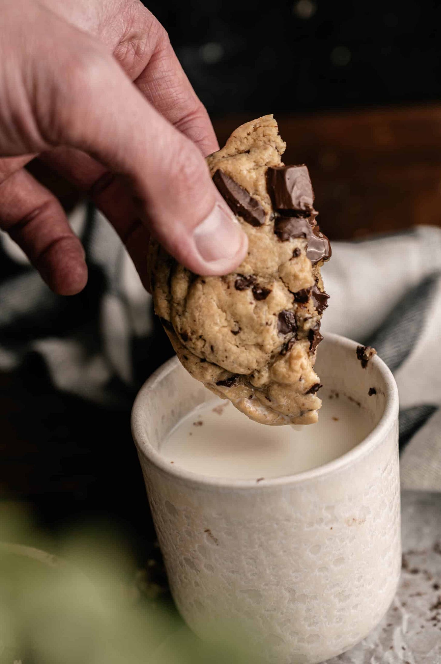 a half eaten chocolate chip cookie being dunked into a glass of milk.