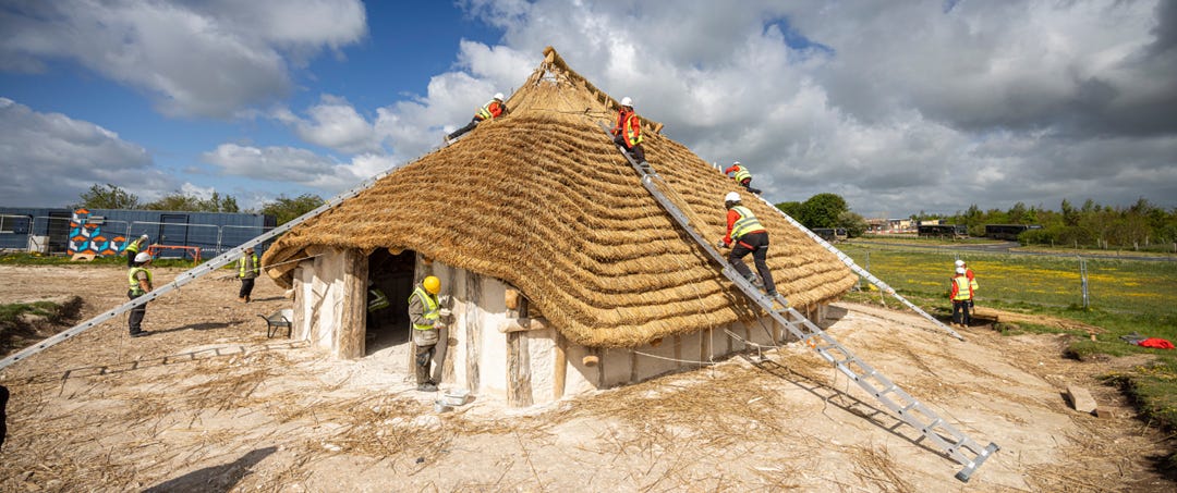 A thatched pre-historic white house with ladders extended onto the roof and people in high vis working on the roof