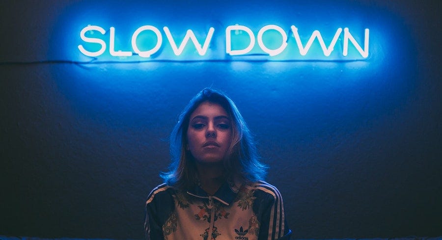 Young woman under neon sign "Slow Down" Young woman under neon sign "Slow Down"