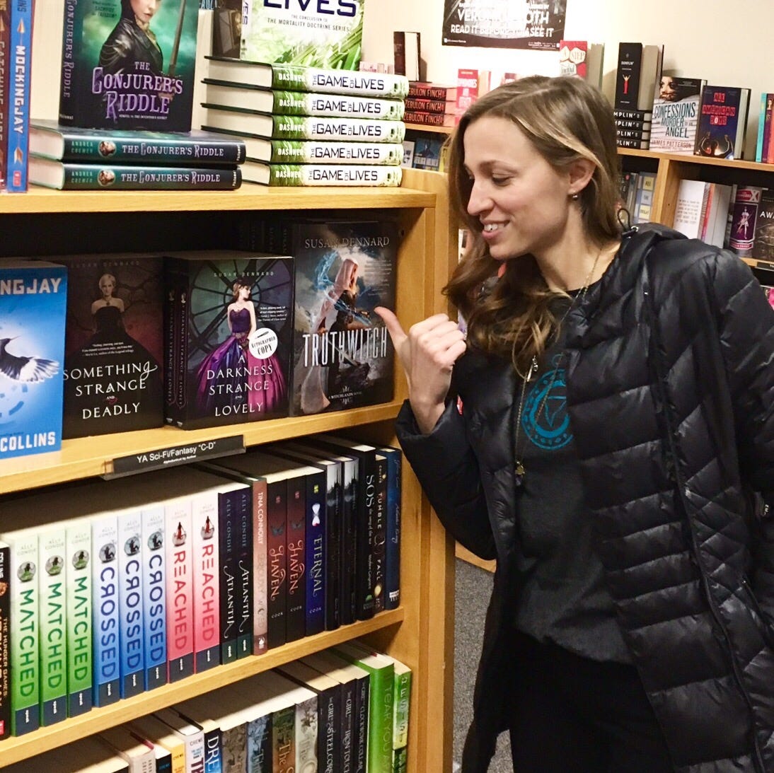 A photo of Susan at a bookstore pointing to the hardcovers of Truthwitch on the shelf next to her other titles, Something Strange & Deadly and A Darkness Strange & Lovely A photo of Susan at a bookstore pointing to the hardcovers of Truthwitch on the shelf next to her other titles, Something Strange & Deadly and A Darkness Strange & Lovely
