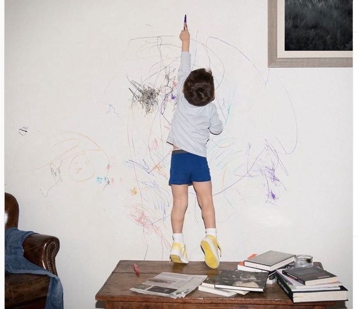 This may contain: a young child is drawing on the wall with chalk and crayon markers in his room