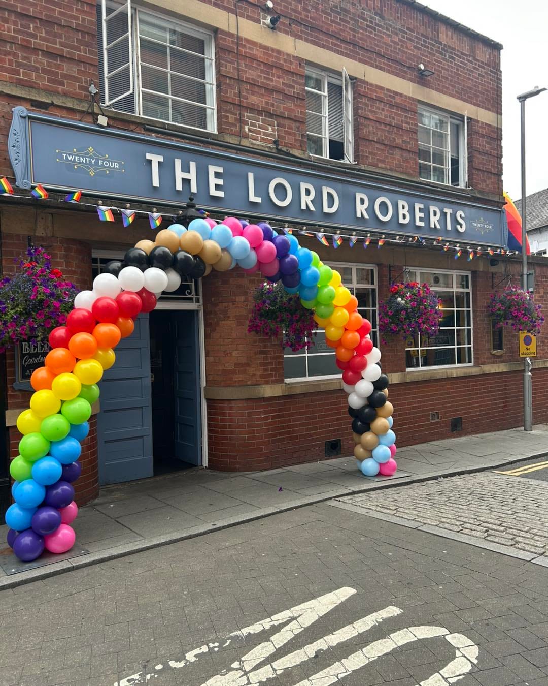 Exterior of The Lord Roberts pub, with a rainbow balloon arch framing the entrance and Pride bunting along the frontage.