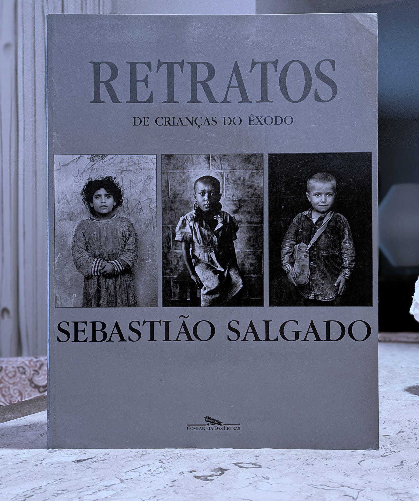 Photo of the book by Sebastião Salgado. It shows three black and white photos of refugee children on the cover.