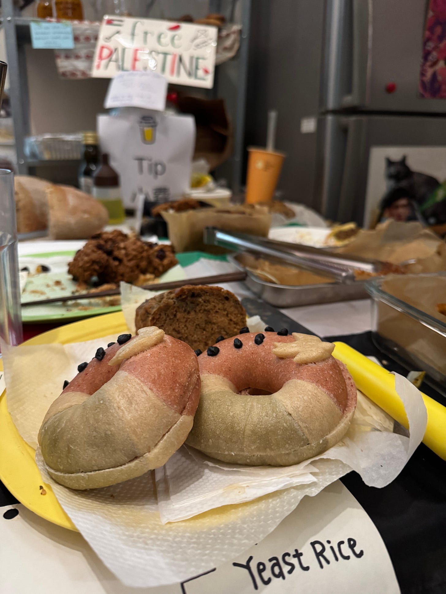 Vertical photo of a bake sale table with bagels visible in the foreground, in the design of Palestine motifs, with hand-written sign out of focus in the background reading Free Palestine