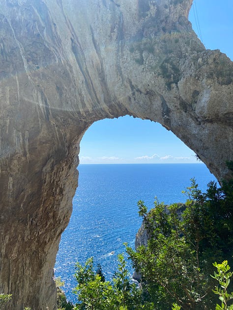 A gallery of three images of rock formations providing different views down to the Mediterranean Sea that surrounds the island of Capri. The rock formations provide different frames looking down from a high point on the island to the water below and the trees that line the images, peeking their green in. The sun shines from different angles in the different pictures.