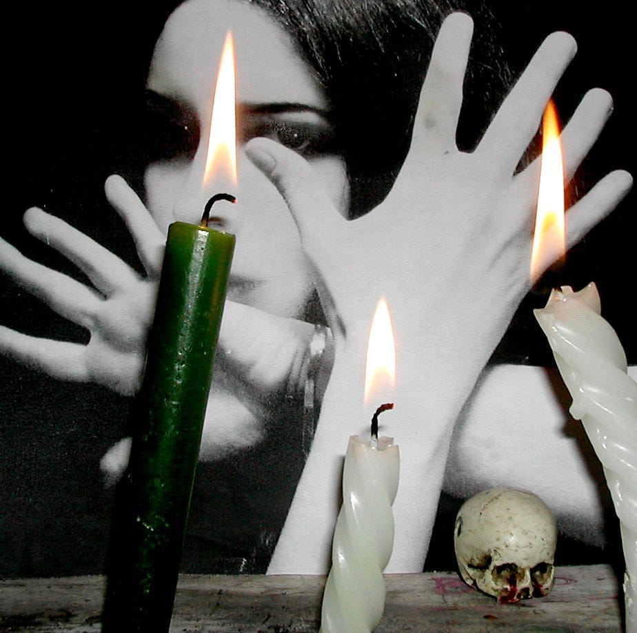 witchy-looking woman with her hands splayed in front of her face and candles in the foreground (once and future witches)