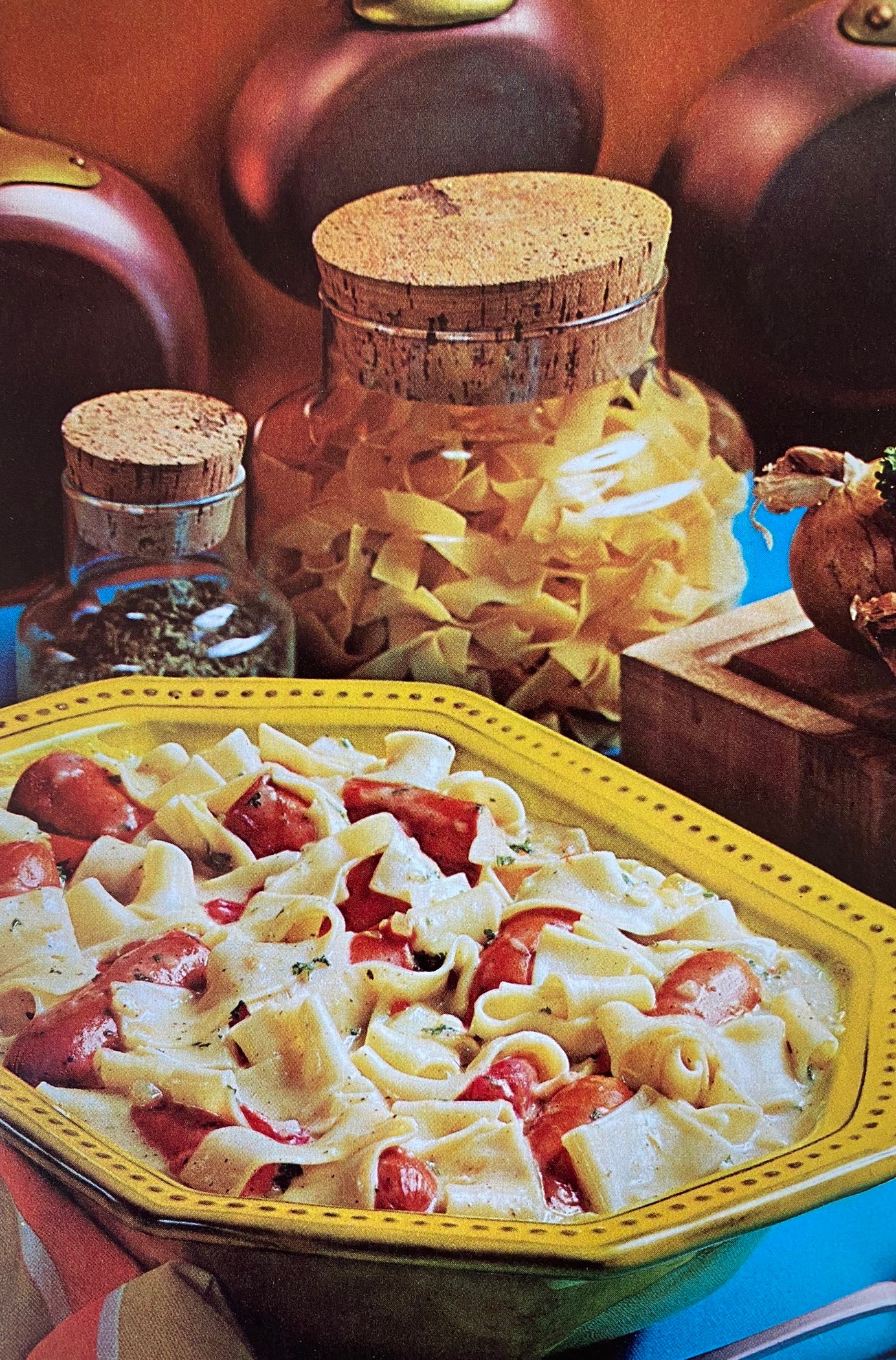 Skillet franks and noodles dish next to glass jars of pasta and herbs.