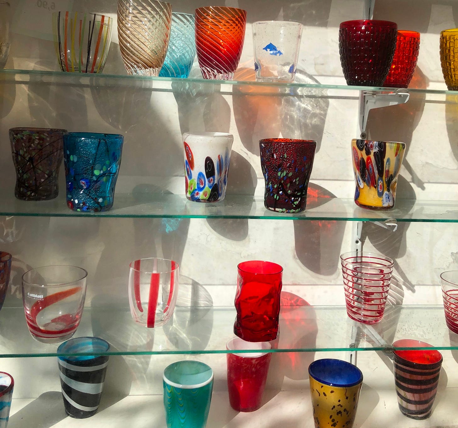 Colorful Murano glasses on glass shelves.