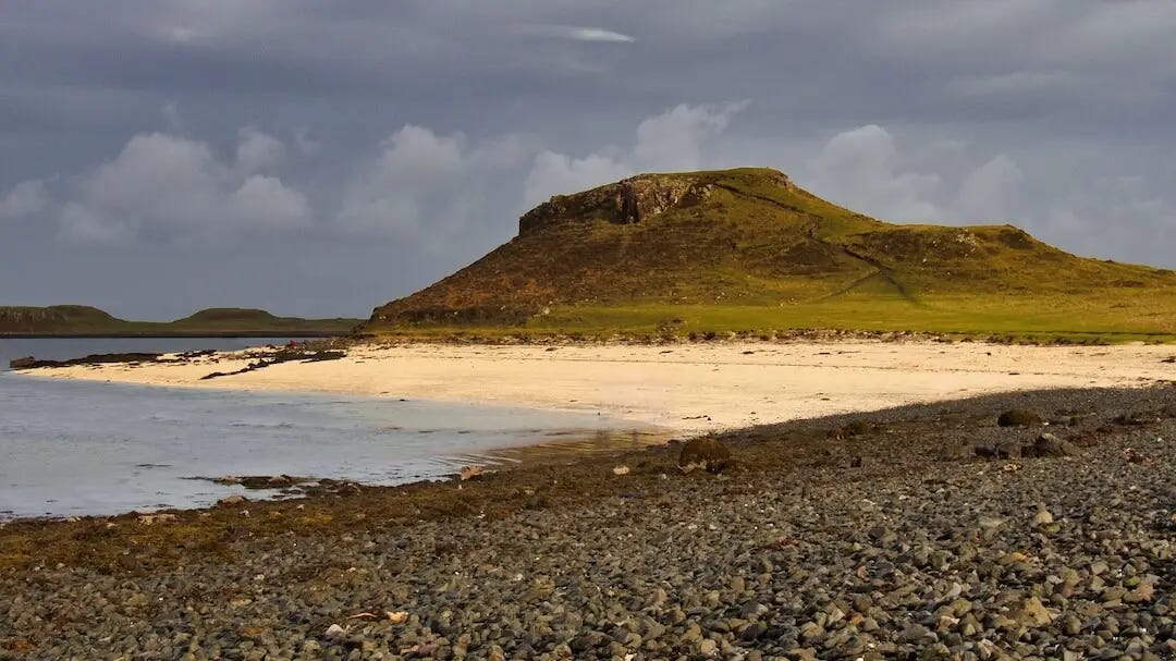 A pebbly beach in the foreground and a white powder beach in the background