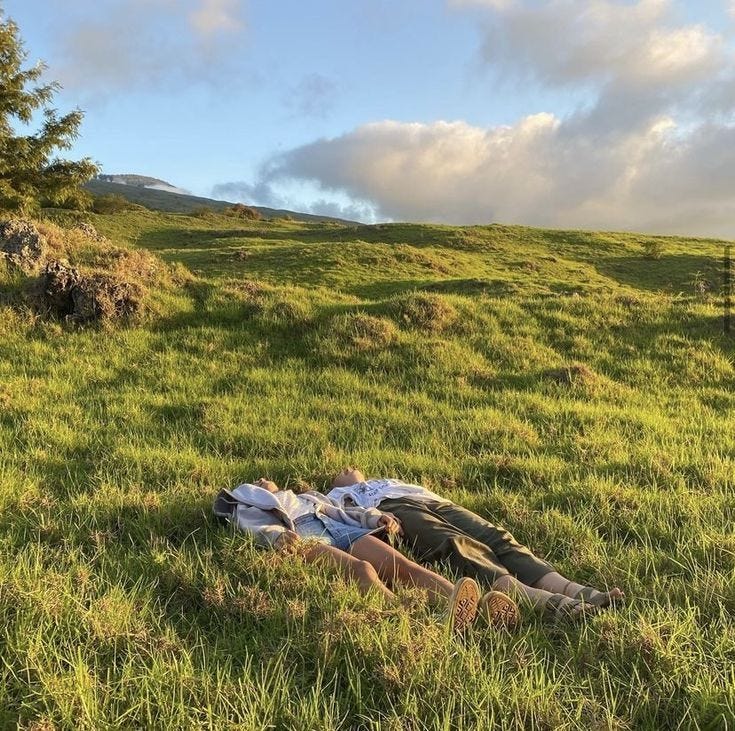 This may contain: two people laying in the grass on top of a hill