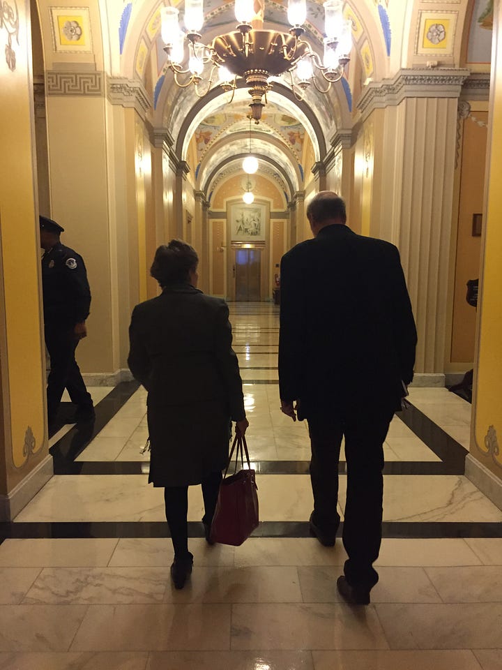 Nine images from a trip to the U.S. Capitol. Picture #1: a woman and a man walking through the halls of Congress. Picture #2 The Capitol rotunda. Picture #3: A woman and a man admiring art on a wall. Picture #4: Memoir coach Christine Wolf in the National Archives. Picture #5 a sign in an elevator of the House of Representatives, Picture #6: a man walking through a hallway. Picture #7 a view of the capitol from a window. Picture #8 Two elevator doors. Picture #9: a hallway with ornate ceilings.