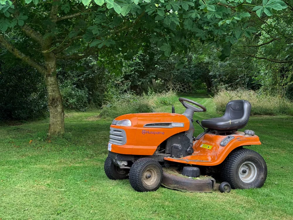 an orange ride on mower sits in the garden between roaring