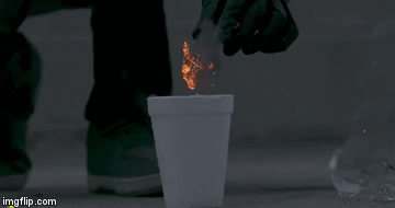 A ground-level image of someone dropping burning steel wool into a styrofoam cup. The styrofoam cup does not merely catch on fire, but fire explodes in curling tendrils in all directions with an explosion like the bursting of the top of a volcano out of the cup’s mouth. A ground-level image of someone dropping burning steel wool into a styrofoam cup. The styrofoam cup does not merely catch on fire, but fire explodes in curling tendrils in all directions with an explosion like the bursting of the top of a volcano out of the cup’s mouth.