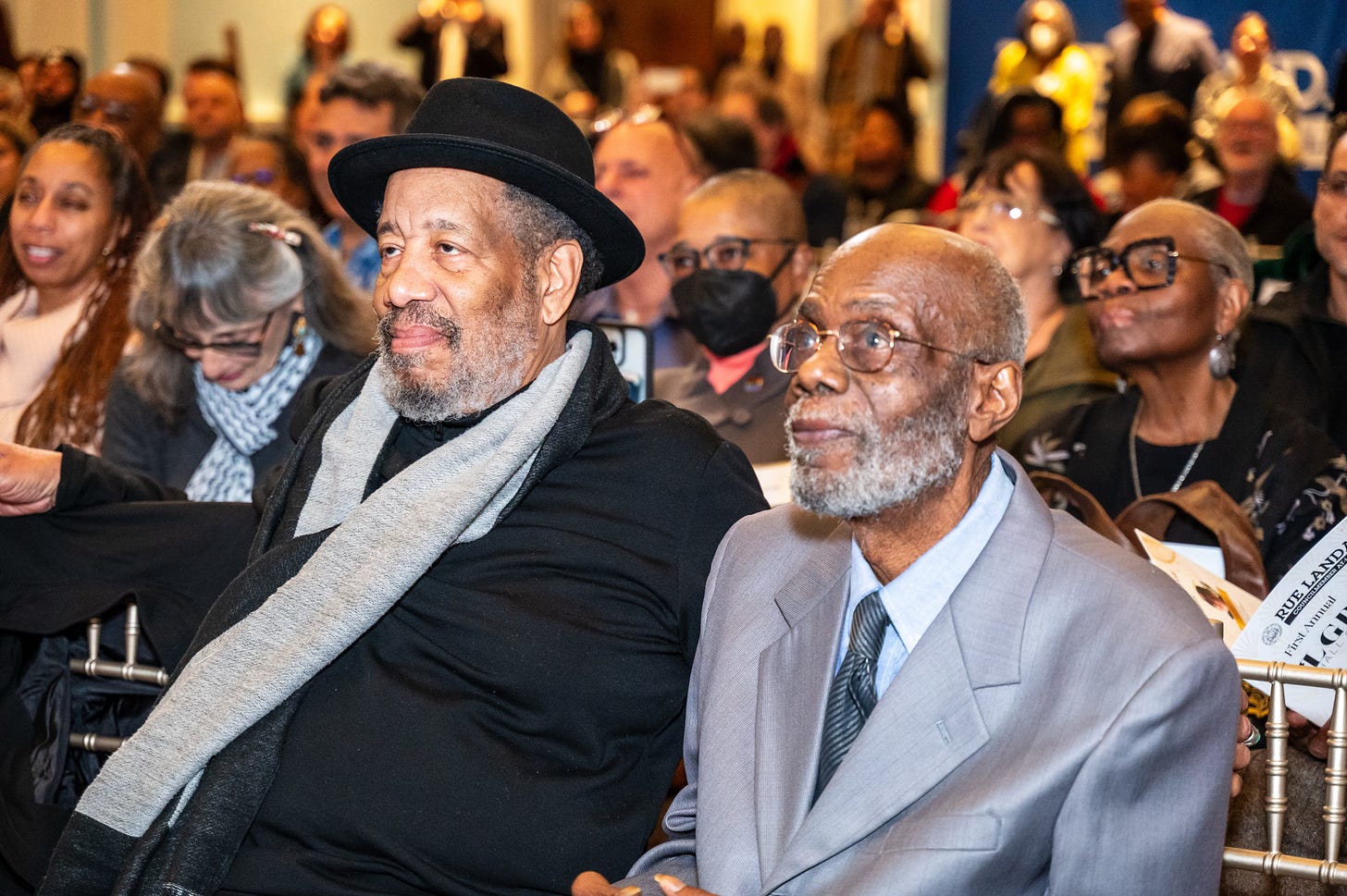 Michael, wearing a black sweater with a gray scarf, sits in the front row to the left of Tyrone, who is dressed in a gray suit, at the Philadelphia LGBTQ+ Hall of Fame Awards ceremony. Michael, wearing a black sweater with a gray scarf, sits in the front row to the left of Tyrone, who is dressed in a gray suit, at the Philadelphia LGBTQ+ Hall of Fame Awards ceremony.