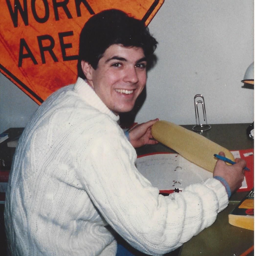 College-aged guy, sitting at a desk doing homework, smiles for the photographer College-aged guy, sitting at a desk doing homework, smiles for the photographer