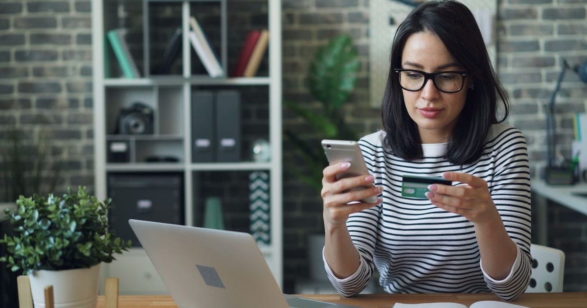 Businesswoman using a smartphone and credit card while working at her laptop. Businesswoman using a smartphone and credit card while working at her laptop.