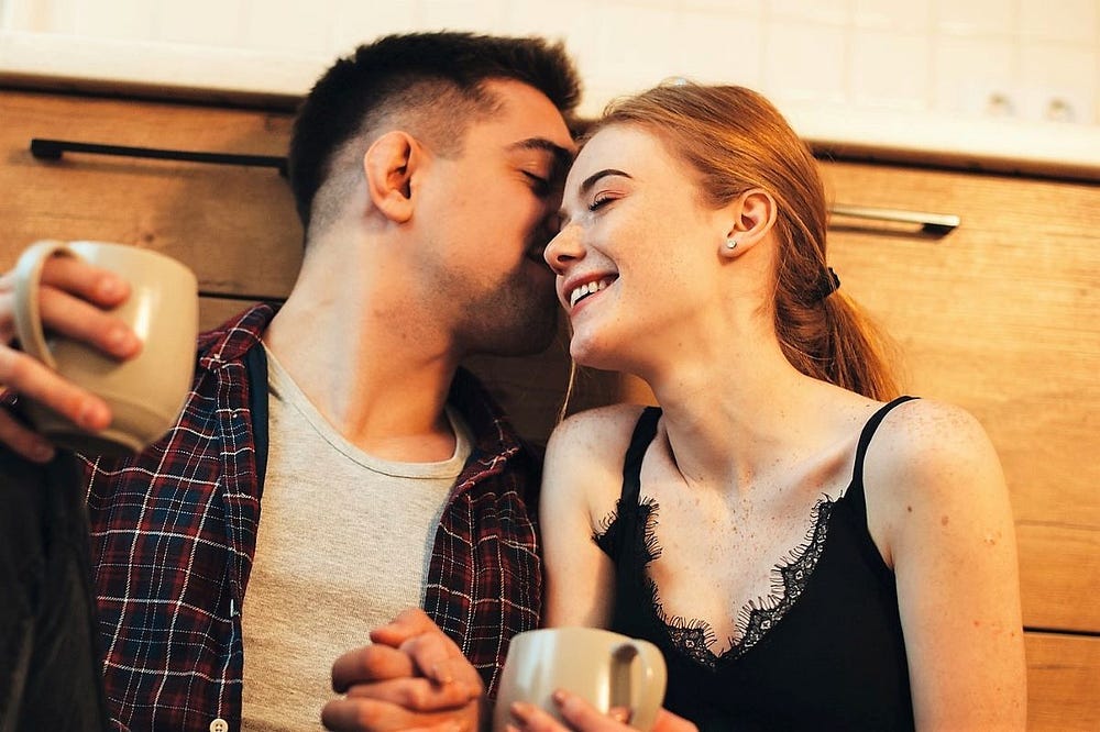 A young red-headed woman smiling and sitting closely with a young man as they share a joke. A young red-headed woman smiling and sitting closely with a young man as they share a joke.