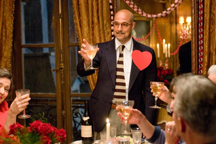 A still from Julie & Julia, in which Stanley Tucci as Paul Child raises a glass as a toast to his wife.