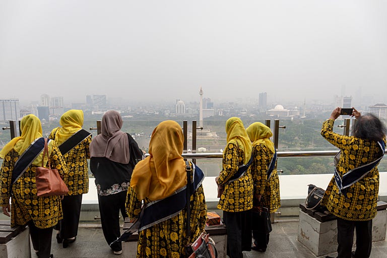 Women wearing yellow and black outfits look out over a polluted Jakarta
