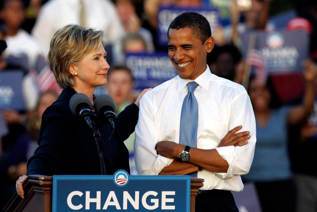 Hillary Clinton and Barack Obama Stand behind a podium featuring Obama's campaign message in 2012