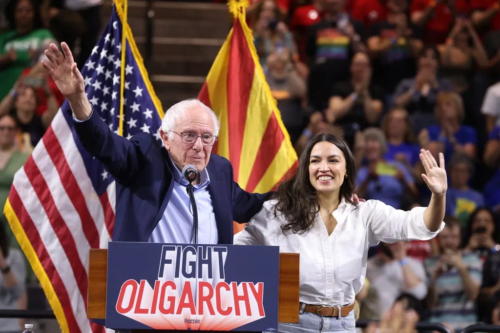 Bernie Saunders and Alexandria Ocasio-Cortez wave to a massive rally.