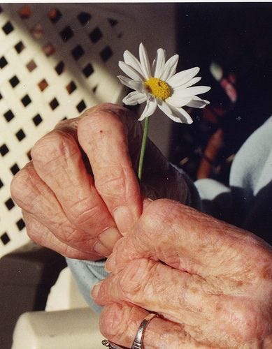 This may contain: an old woman holding a flower in her hands