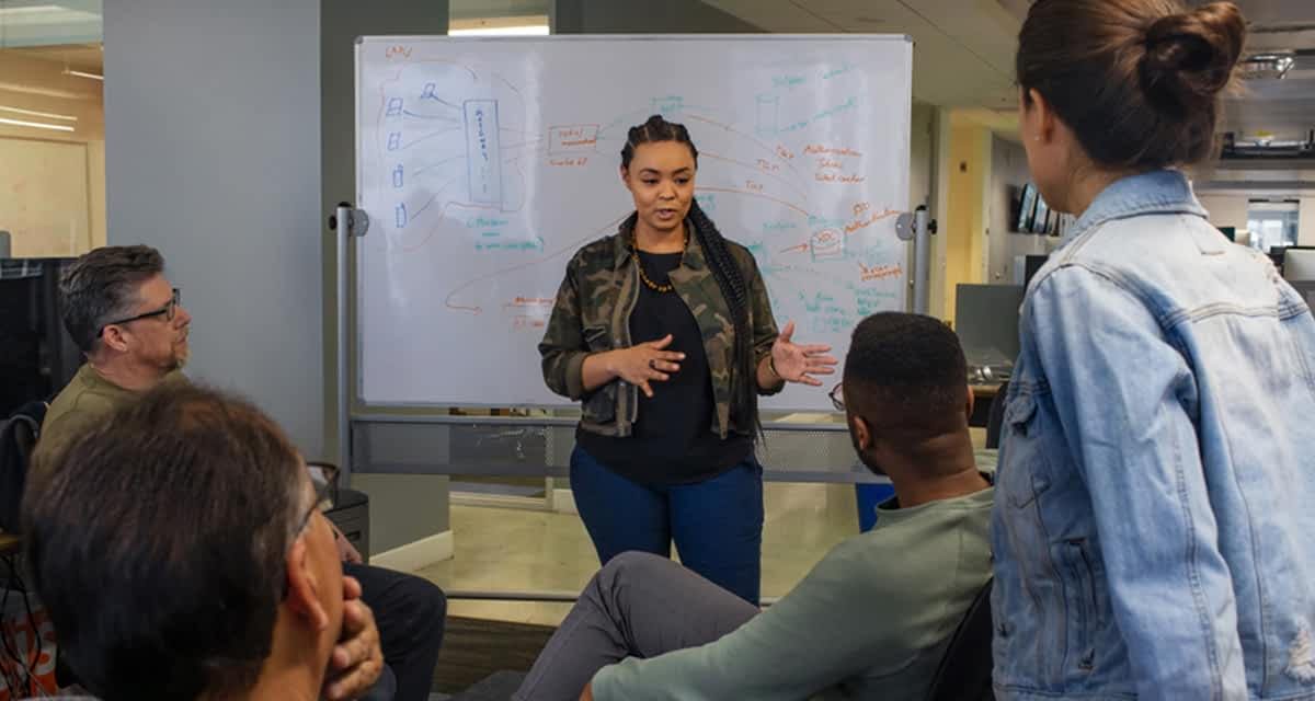 A teacher stands in front of a white board and lectures the class.